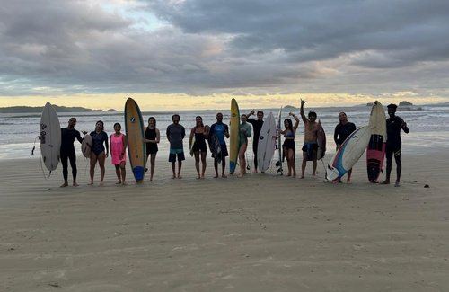 Turma de alunos com pranchas na praia ao entardecer